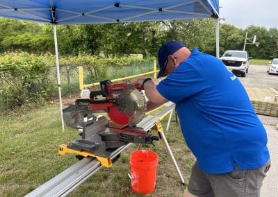 A Cipriani Remodeling Solutions team member wearing a blue shirt operates a circular saw under a canopy as part of a ramp renovation project at the Boys & Girls Clubs of Gloucester County, Inc., Paulsboro Teen Center.
