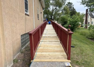 A newly renovated wooden wheelchair ramp with red handrails at the Boys & Girls Clubs of Gloucester County, Inc., Paulsboro Teen Center, completed by Cipriani Remodeling Solutions.