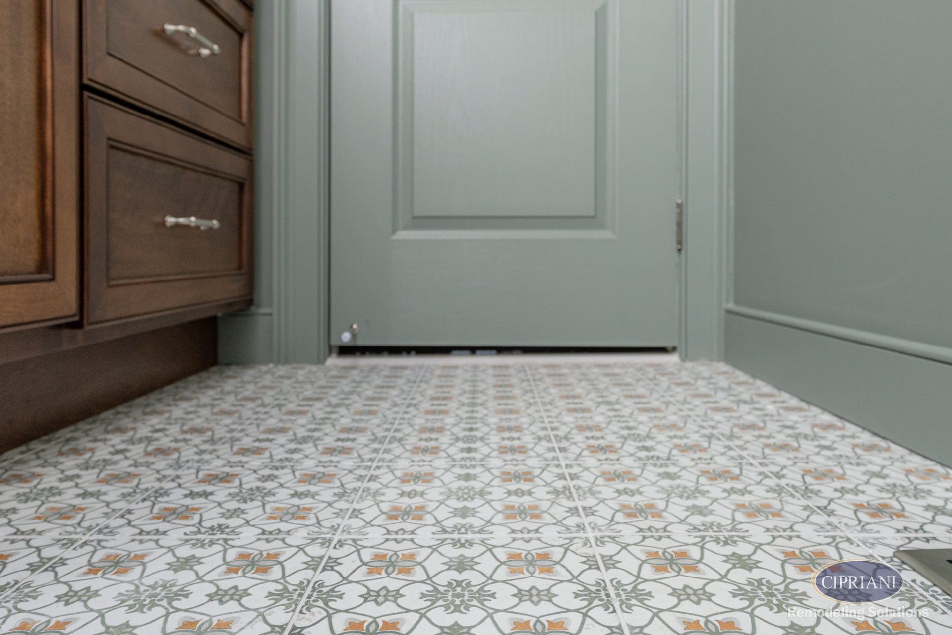 Patterned bathroom floor tile leading to sage green door
