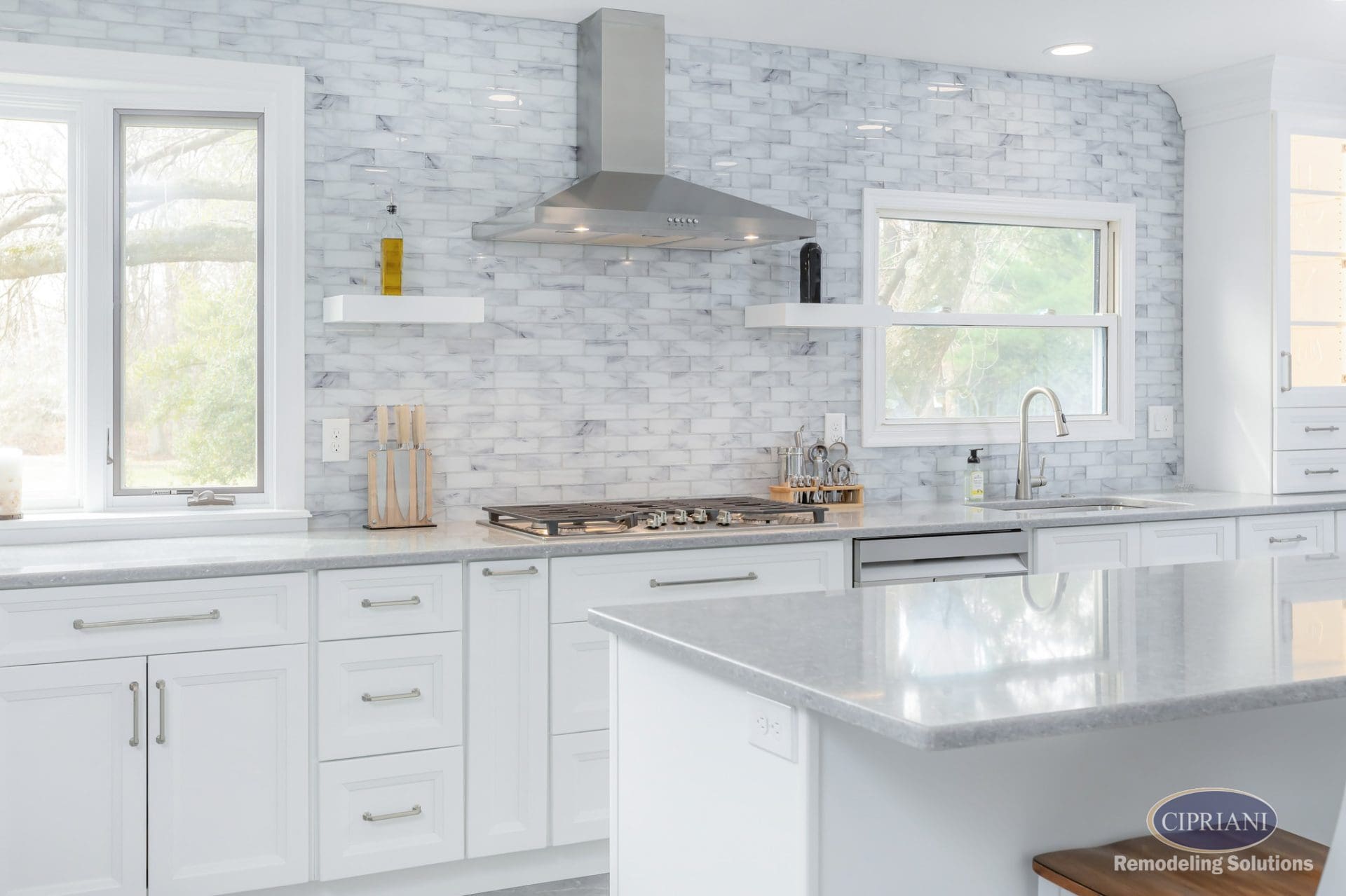 Sleek white kitchen with stainless steel range hood and subtle backsplash