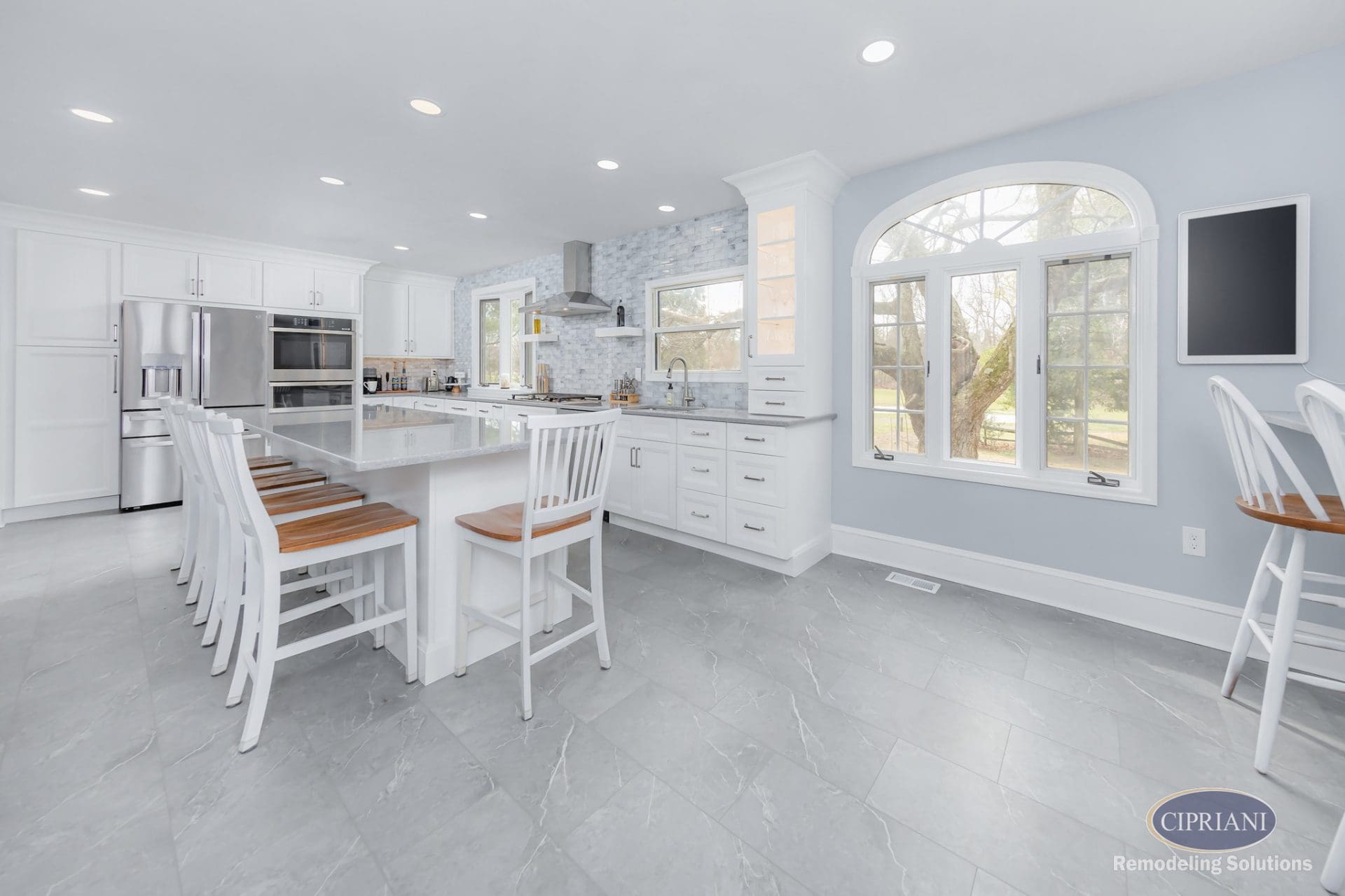 Wide view of modern kitchen island, cabinetry, and arched window