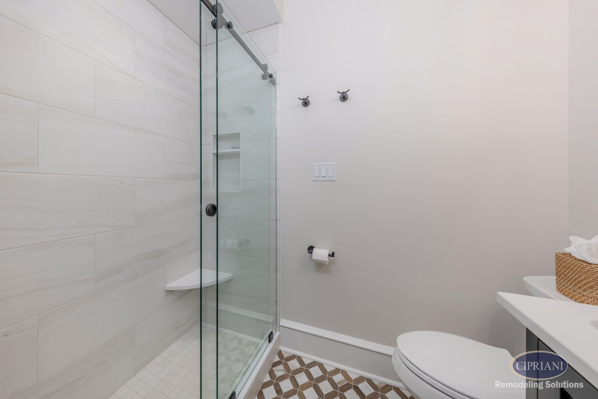 Compact bathroom with glass shower enclosure, large-format tile walls, and geometric tile flooring.