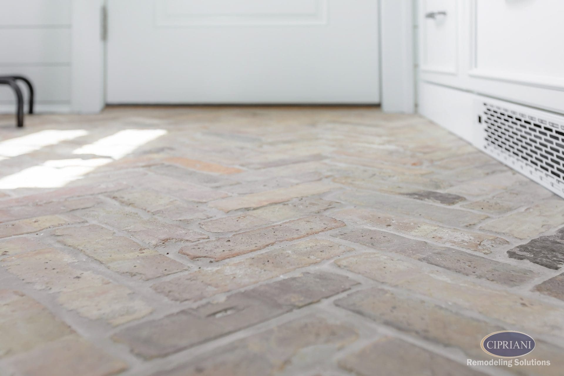 Low-angle view of herringbone brick flooring in a sunlit mudroom entry.