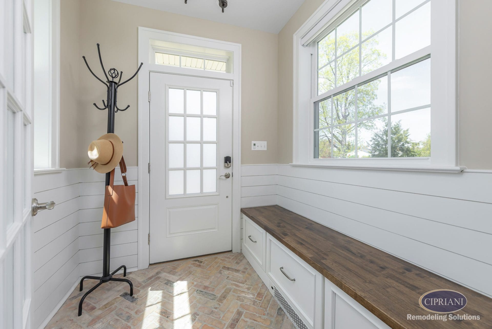 Bright mudroom with bench storage, shiplap walls, and brick herringbone floor.