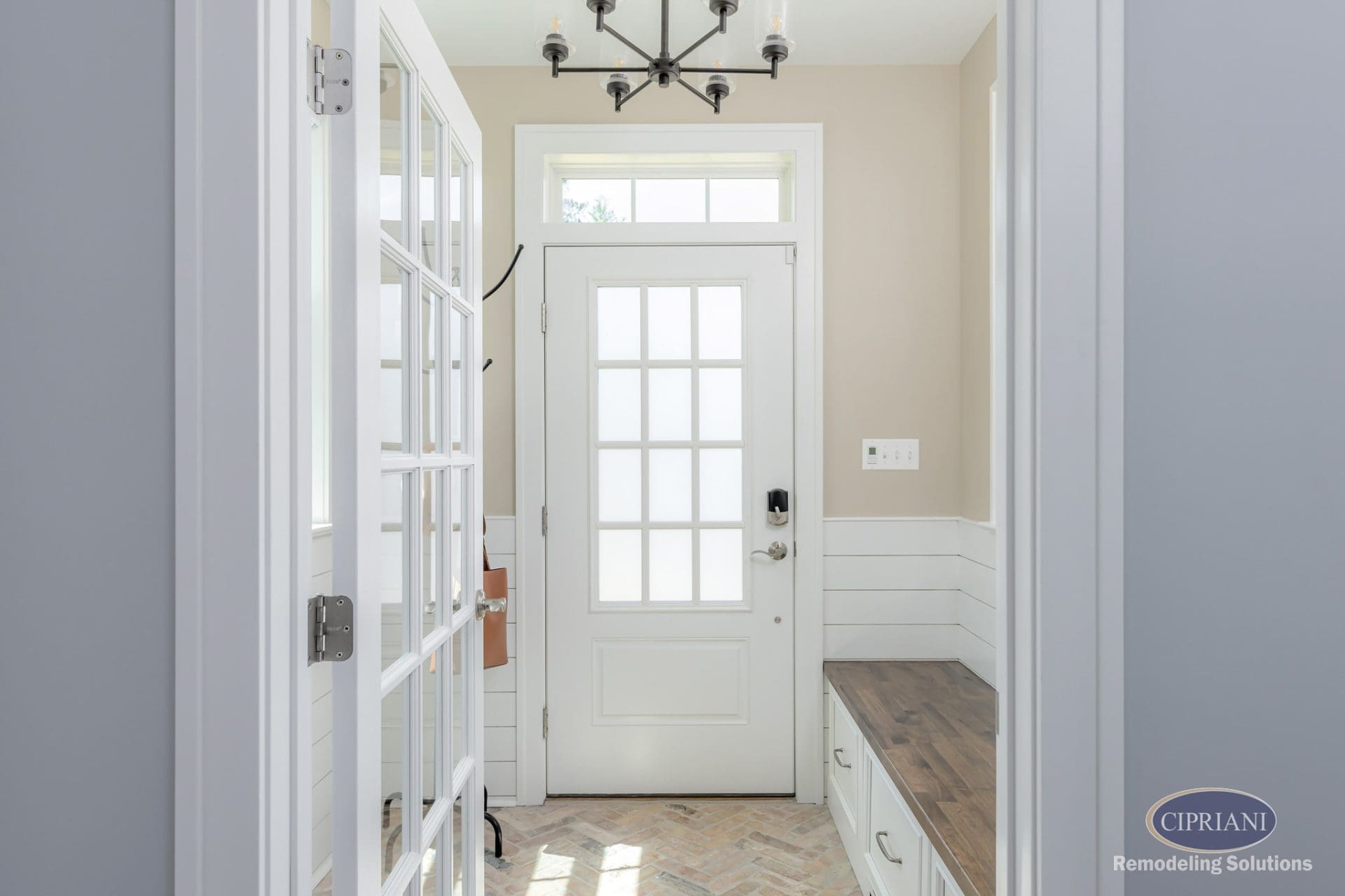 Bright mudroom entry with French door, built-in bench, wood top, and herringbone brick floor.