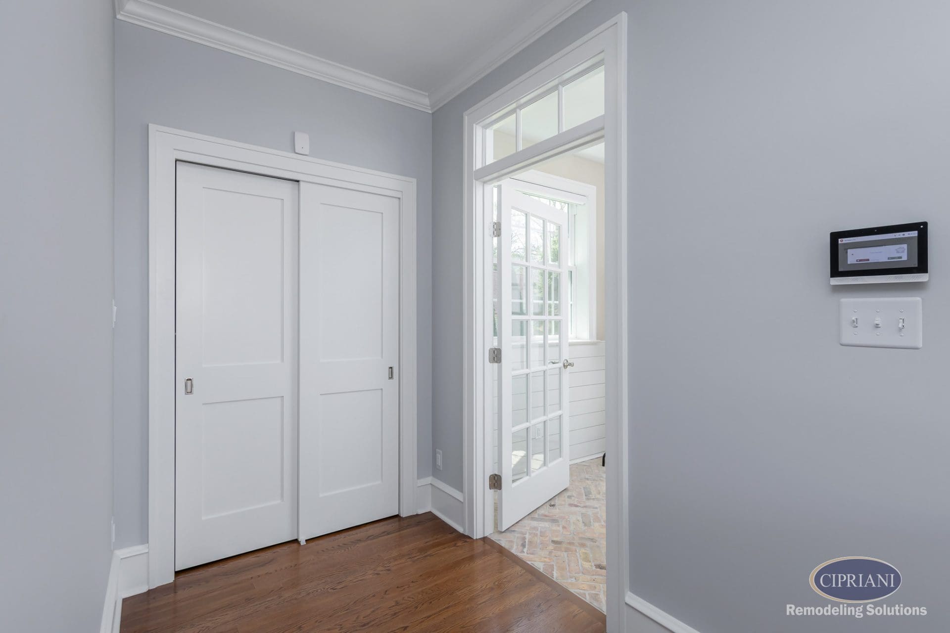 Bright transitional hallway with light blue walls, white trim, and hardwood flooring leading to a brick-tiled mudroom.