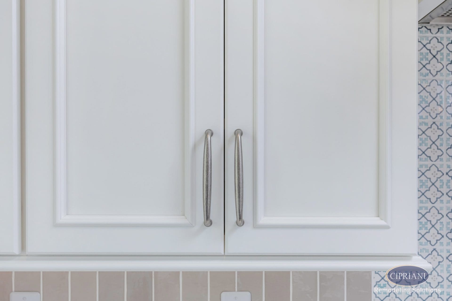Close-up of white raised-panel kitchen cabinet doors with brushed nickel pulls.