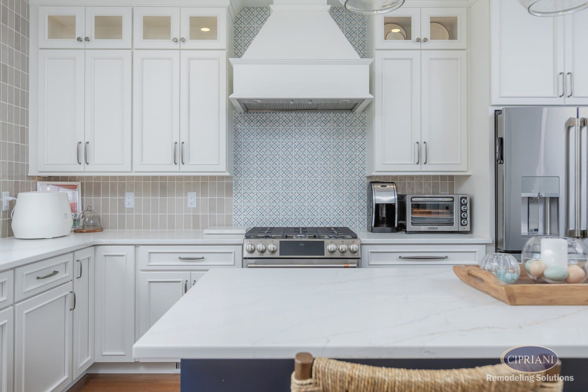 White kitchen with blue patterned backsplash, shaker cabinetry, and quartz island countertop.