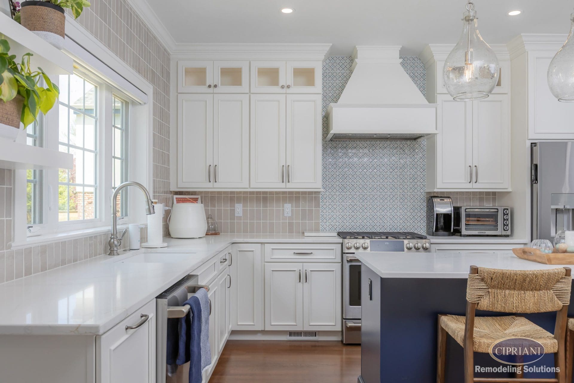 Full view of white kitchen with taupe vertical backsplash, blue accent tiles, and navy island with seating.