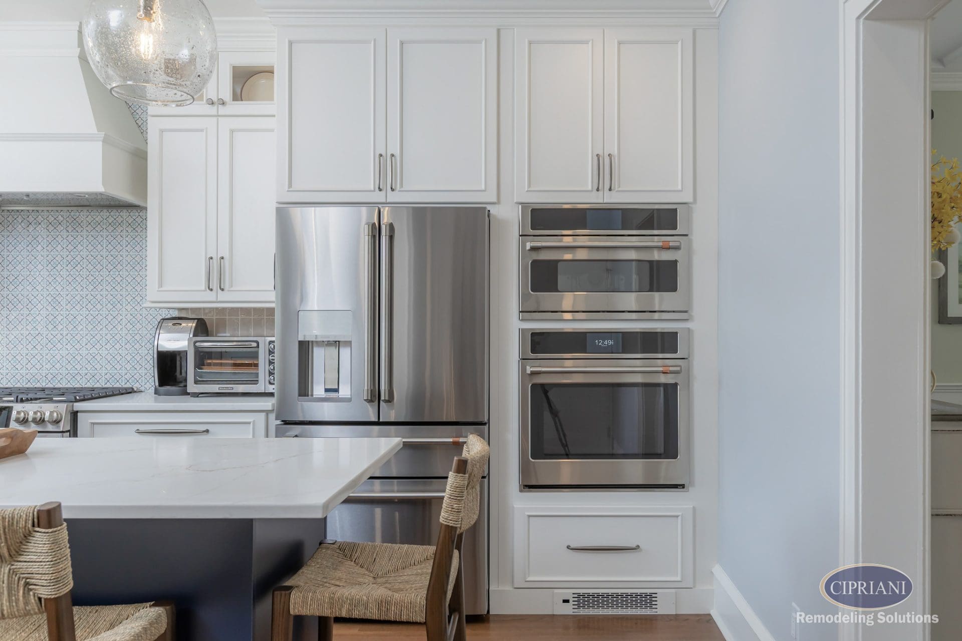 Wall of kitchen appliances with French door refrigerator, stacked ovens, and custom white cabinetry.