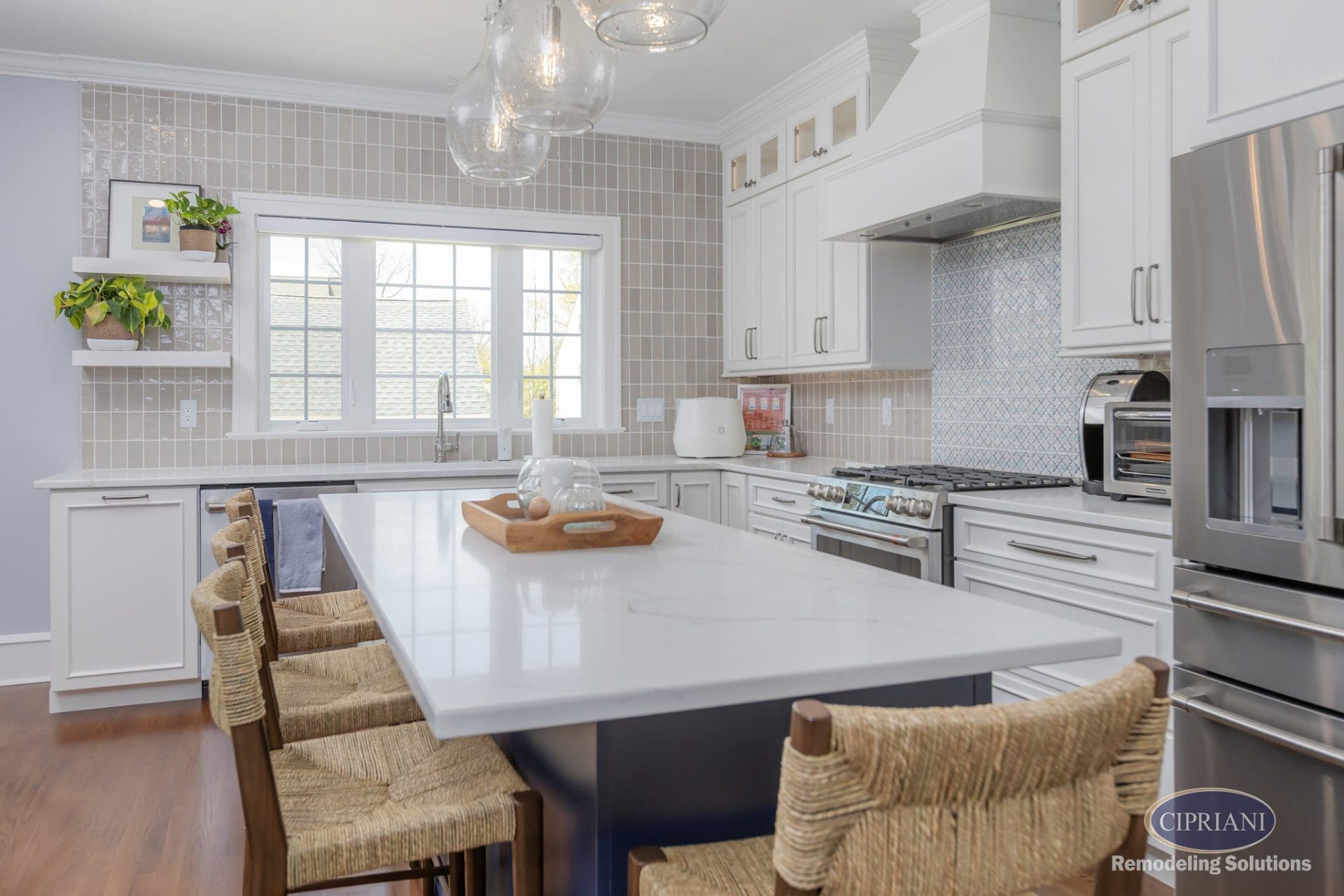 Bright kitchen with white cabinets, blue island, and woven bar stools beneath clear glass pendant lights.