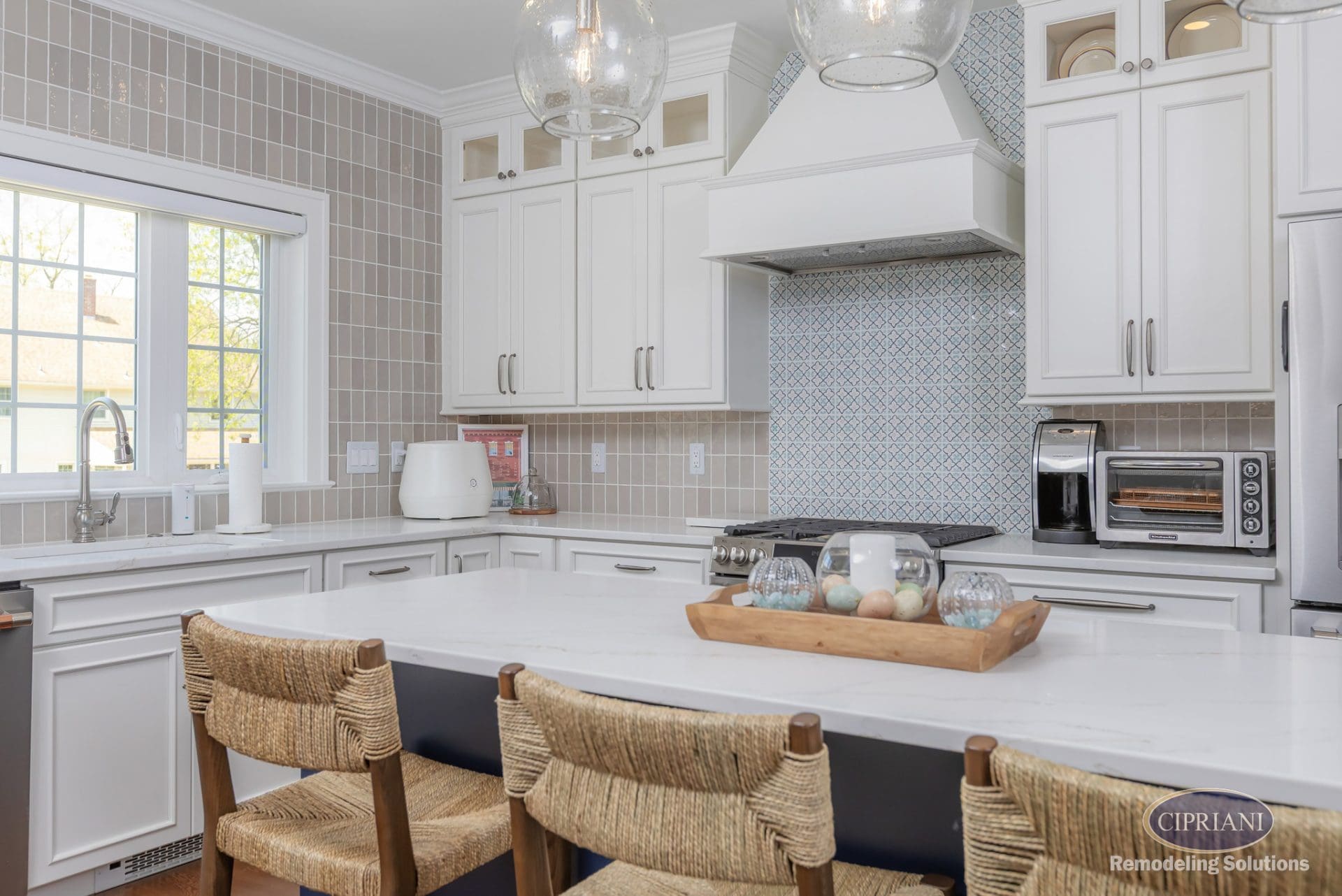 Kitchen with white cabinetry, textured tile backsplash, and a navy island with woven bar stools and pendant lighting.