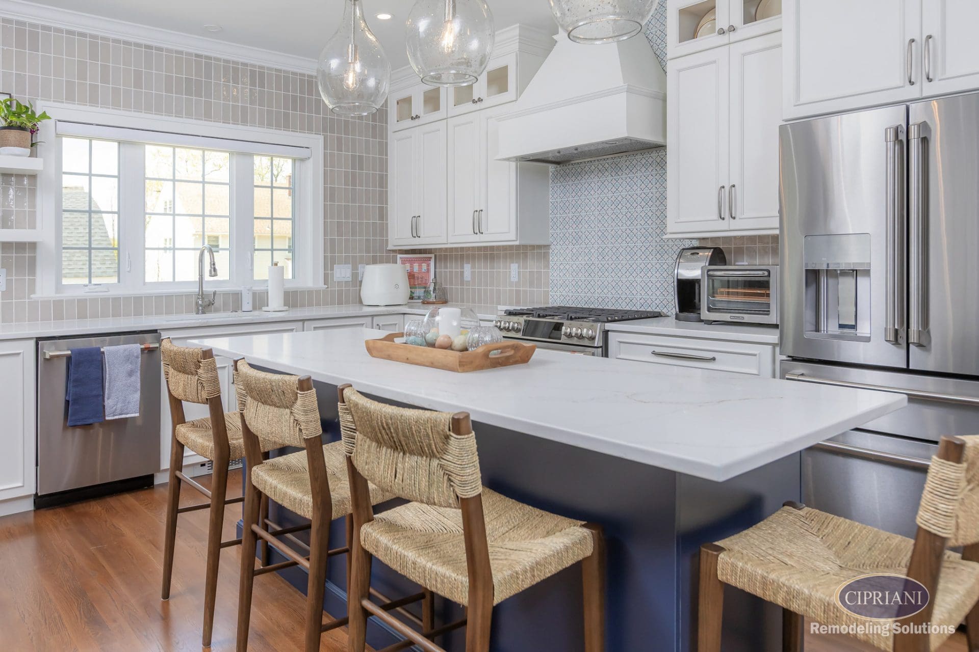 Bright kitchen with navy island, white cabinets, patterned backsplash, and natural wood bar stools under globe pendant lights.