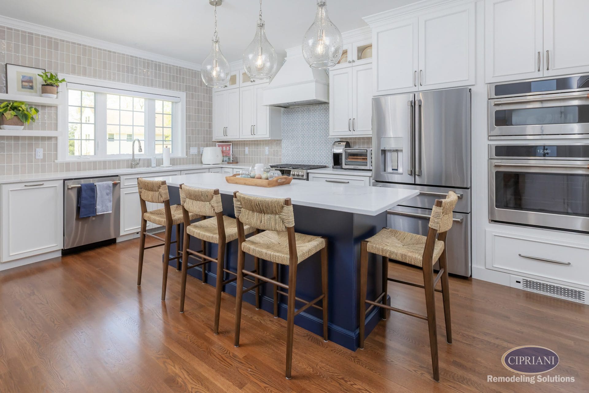 Transitional kitchen with navy island, woven stools, vertical beige tile backsplash, and stainless appliances.