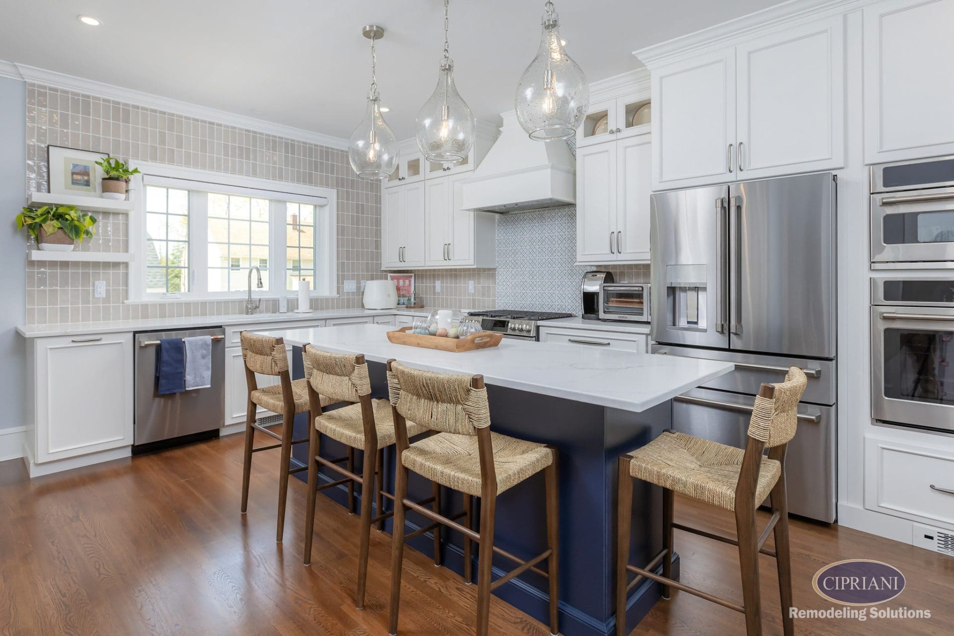 Wide-angle view of a bright kitchen with white cabinetry, a navy island, and mixed tile backsplashes.