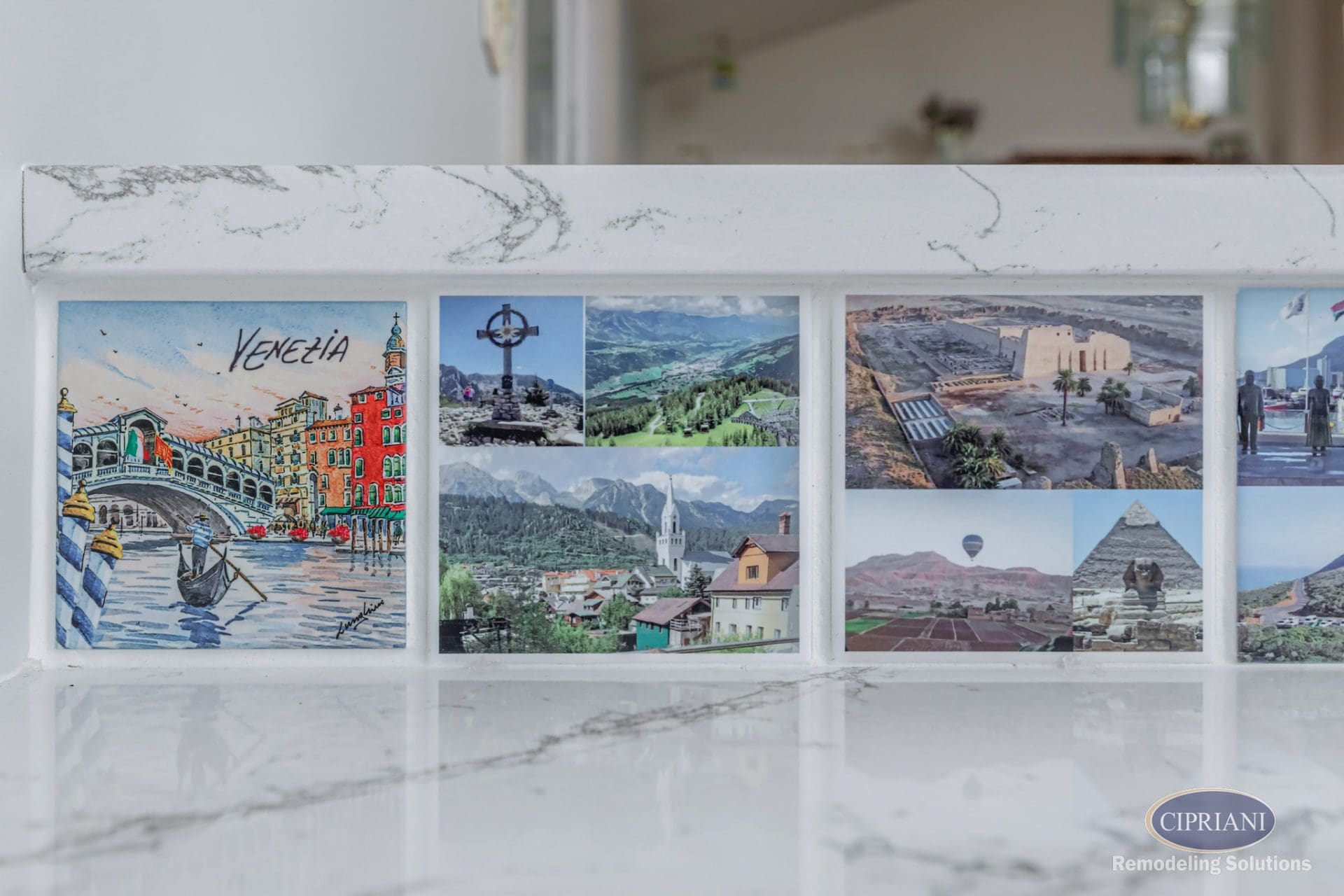 Close-up of custom tile backsplash featuring postcards and travel photos embedded in white marble.