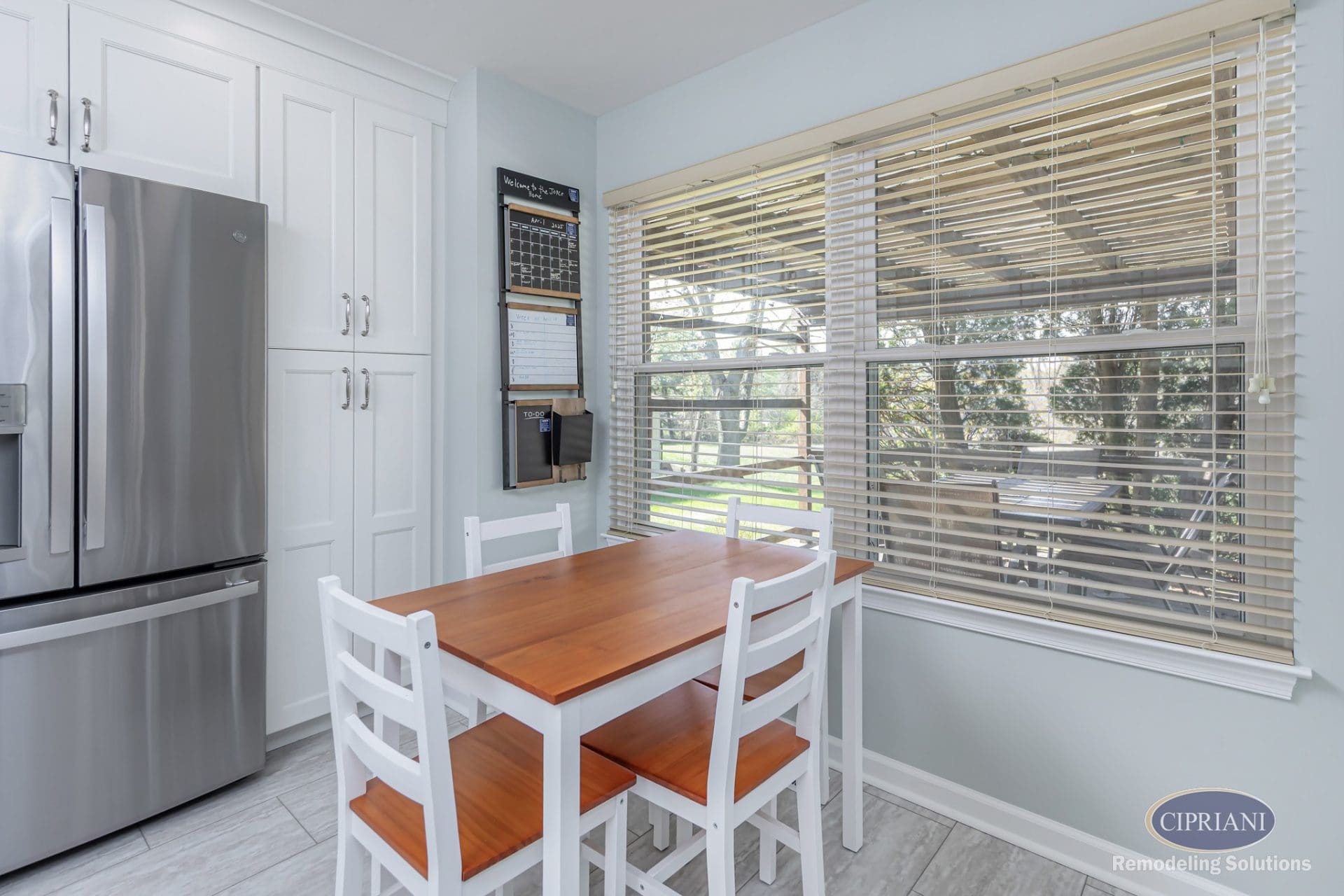 Bright breakfast nook with wood-top dining table, wall calendar, and large window overlooking patio.