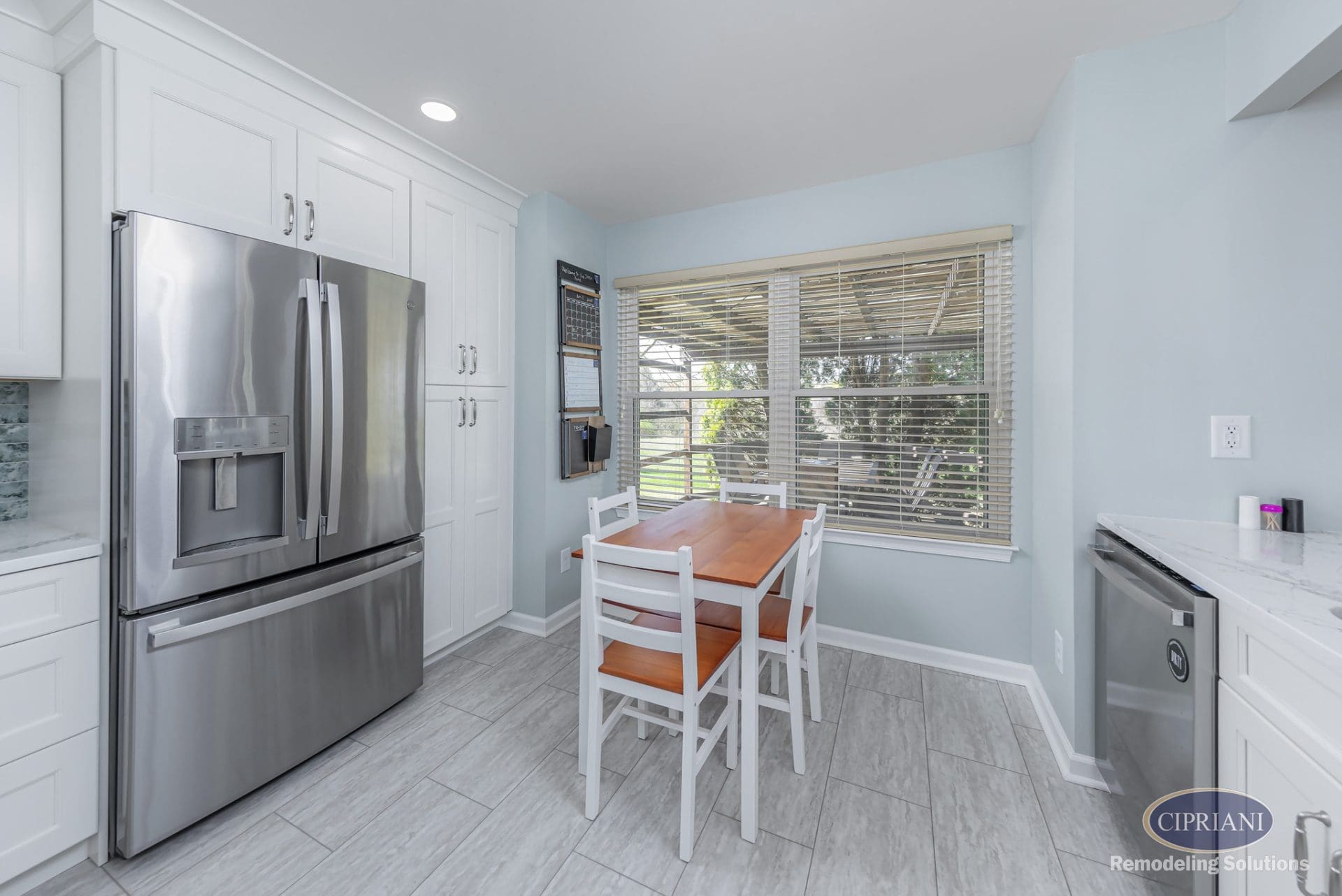 Kitchen corner with stainless steel refrigerator, white cabinetry, and wood-top breakfast table.