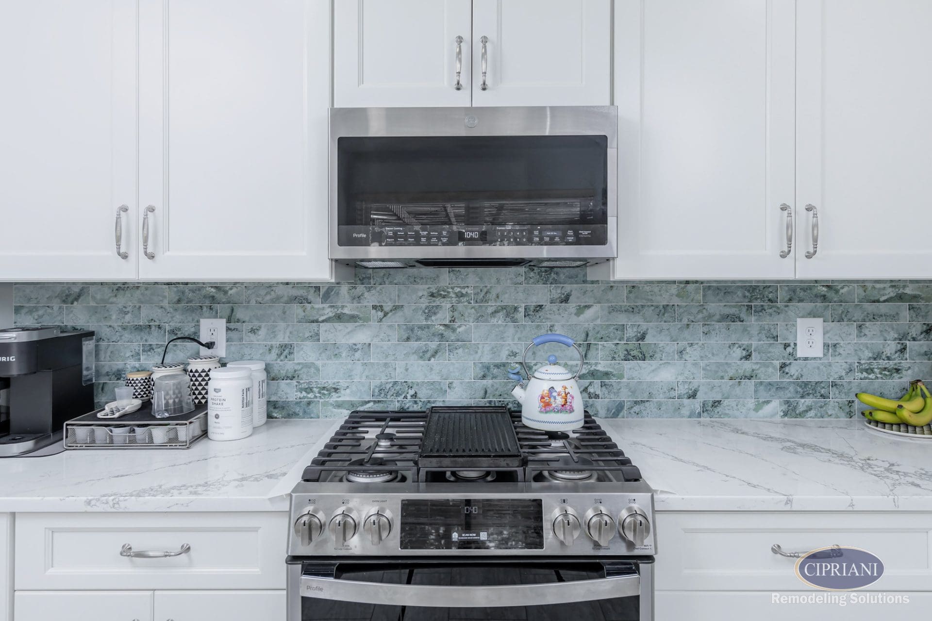 Stainless steel range and microwave with seafoam green tile backsplash and white cabinetry.