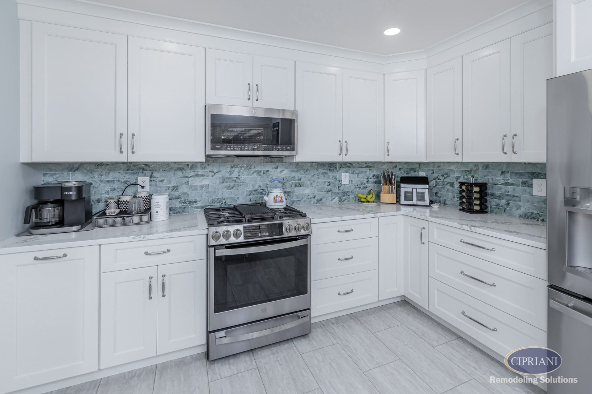 Modern white kitchen with stainless appliances, seafoam green backsplash, and shaker cabinetry.