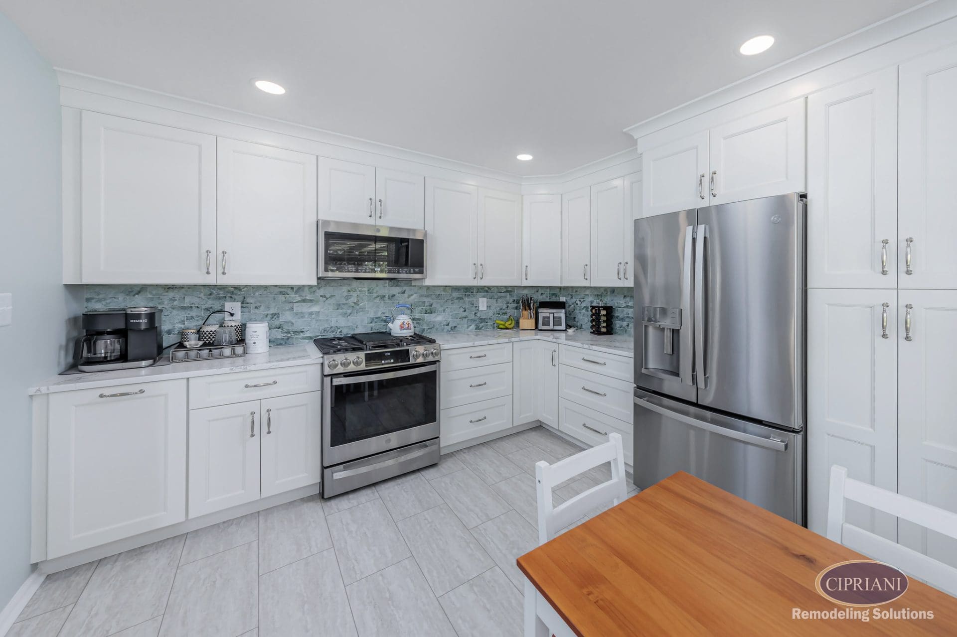 Full view of white kitchen with stainless appliances, textured green backsplash, and wood dining table.