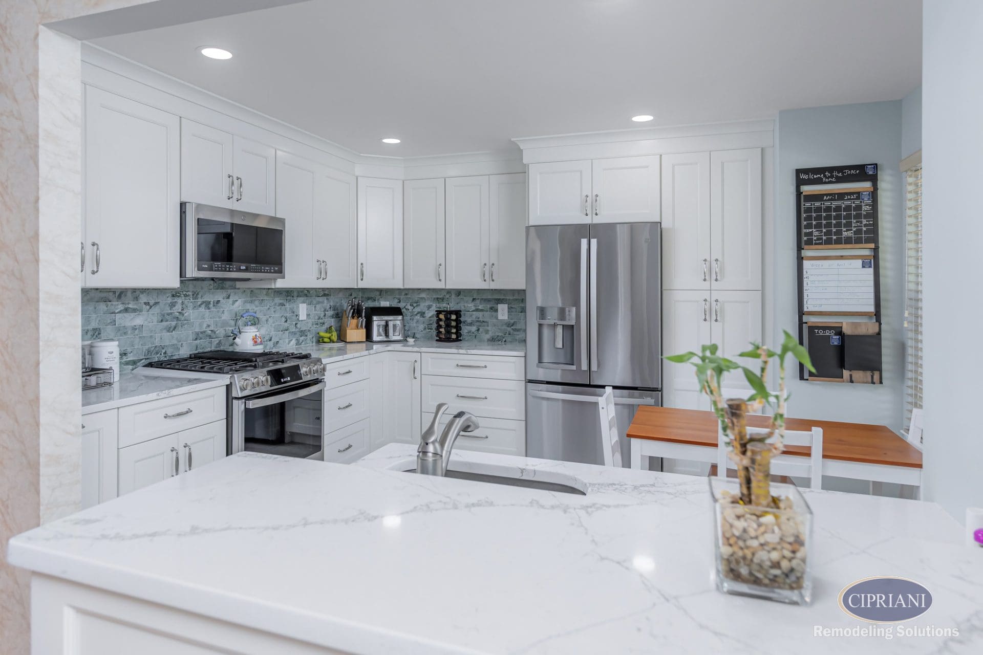 View of white kitchen from peninsula with marble countertop and stainless fixtures.