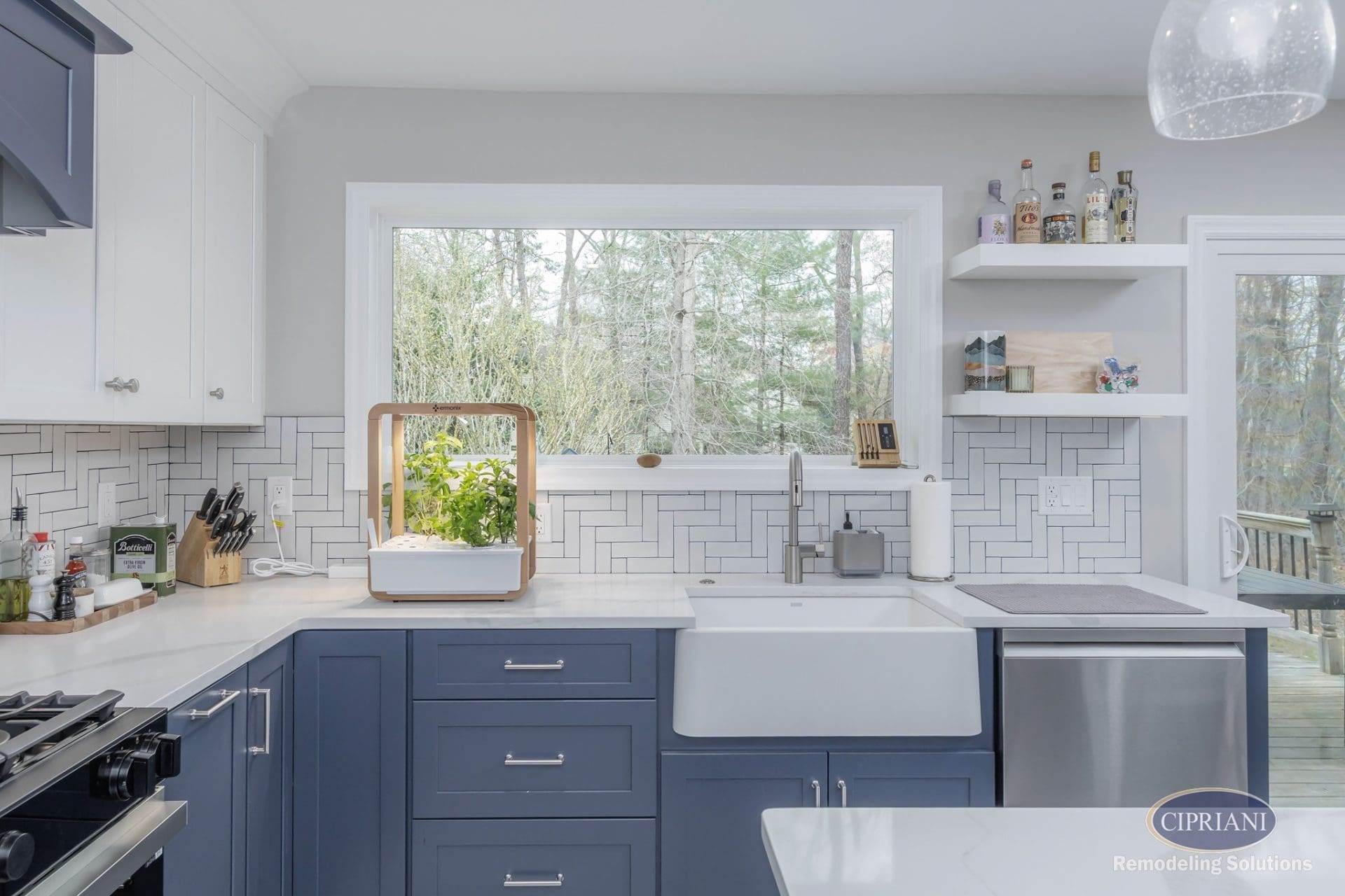 Kitchen sink with blue base cabinets, large window, herringbone backsplash, and indoor herb garden.