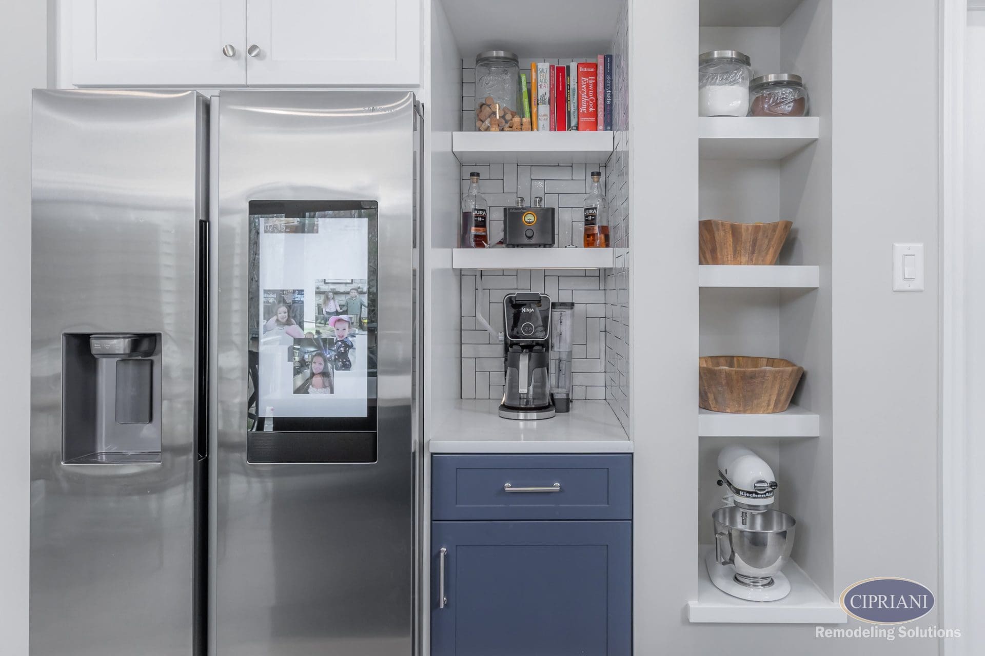 Coffee station and shelving nook beside smart fridge with navy base cabinet and white tile backsplash.