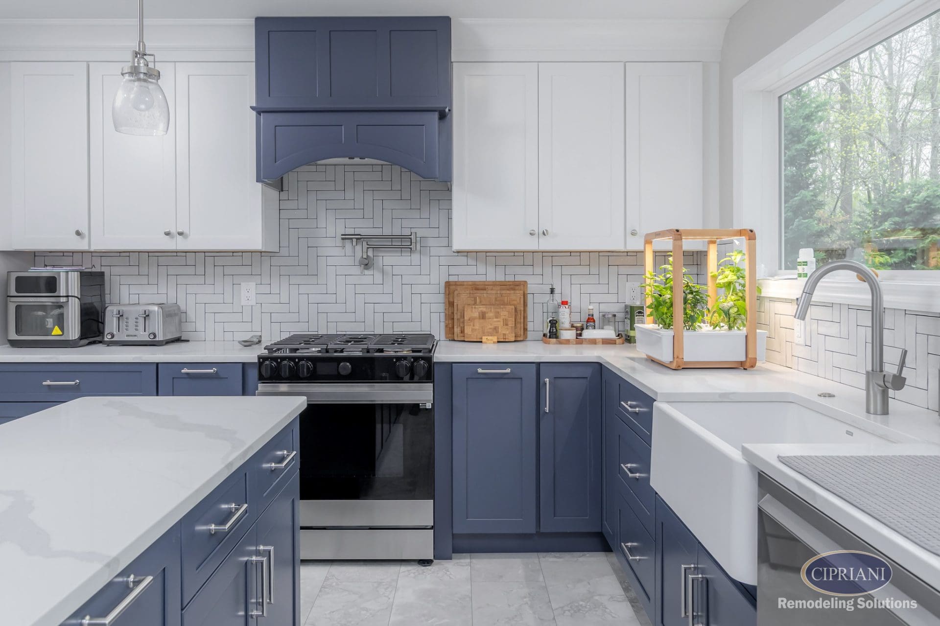 Close-up view of kitchen with navy base cabinets, farmhouse sink, pot filler, and herb garden.