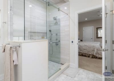 Glass shower with bedroom view – A sleek walk-in shower with glass doors, vertical tile, and built-in niche sits adjacent to a doorway leading into a cozy primary bedroom.