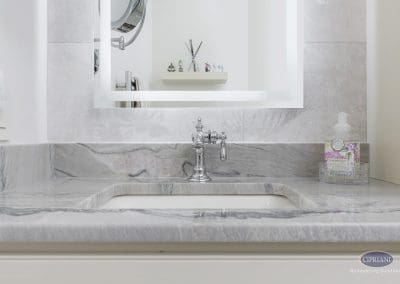 Marble vanity close-up – A close-up of a marble vanity countertop with an undermount sink, polished chrome faucet, and lighted mirror.
