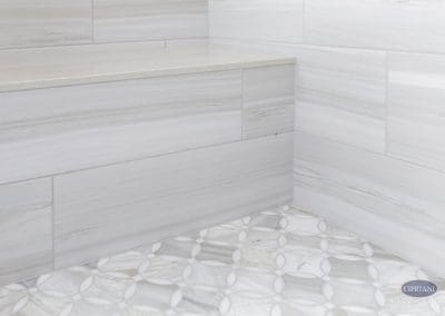 Tile bench with patterned floor – A built-in shower bench wrapped in horizontal tile meets a marble mosaic floor with an interlocking circle design.