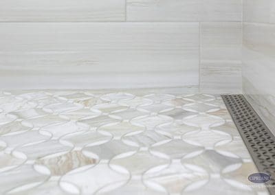 Curved tile shower floor – A close-up of marble shower tile with a flowing wave pattern and a sleek linear drain inset into the corner.