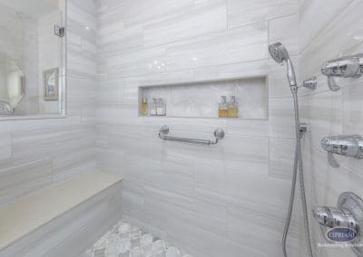 Walk-in shower with bench and handheld sprayer – A full view of the walk-in shower shows a built-in bench, recessed niche, and chrome body sprays with a handheld showerhead.