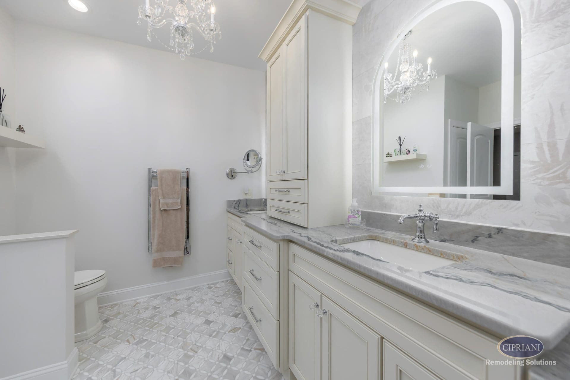 Elegant Cream Vanity with Marble Countertops | Cipriani Remodeling Solutions Elegant double vanity – A refined cream-colored vanity with marble countertops and chrome fixtures beneath a glowing arched mirror and crystal chandelier.