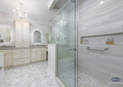 Full bathroom view – A spacious bathroom featuring a large walk-in glass shower, dual vanities with arched mirrors, crystal chandelier, and patterned tile flooring.