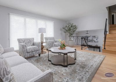 Light-filled living room with staircase – A spacious living room with pale wood floors, layered textures, and a sculptural coffee table sits beside a staircase with black iron railing.