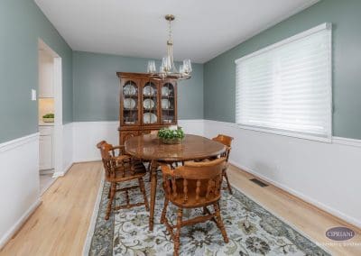 Traditional dining room with green walls – A cozy dining room features a wooden table and chairs, two-tone wall paint, and a modern brass chandelier above.