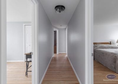 Bright Hallway with Bedroom Views – A long hallway with light hardwood flooring and soft gray walls, leading to multiple bedrooms in a freshly remodeled home.