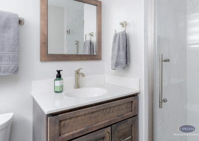 Compact Vanity with Rustic Warmth – A small bathroom vanity with a wood-framed mirror, brushed nickel faucet, and soft gray towels creating a cozy feel.