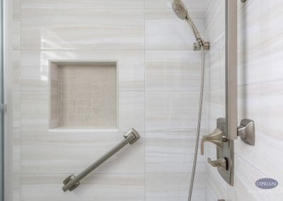 Shower with grab bar and niche – A close-up of a modern shower with a handheld sprayer, angled grab bar, and recessed niche with soft mosaic tile.