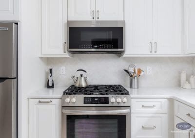 Sleek Stainless Range in White Kitchen – A stainless steel gas range with matching microwave sits between bright white cabinetry and herringbone backsplash.