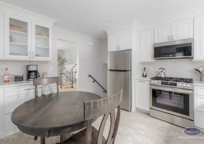 Bright Kitchen with Dining Nook – A cozy round dining table anchors this white kitchen featuring stainless appliances, crown molding, and soft natural light.