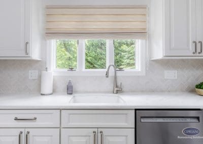 Sink View with Natural Light – A bright kitchen sink setup features a gooseneck faucet, white cabinetry, and a large window with soft Roman shades.