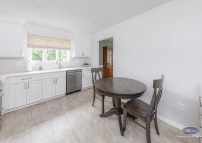 Cozy Eat-In Kitchen Space – A clean white kitchen with stainless steel appliances and a dark wood bistro table creating a welcoming breakfast nook.