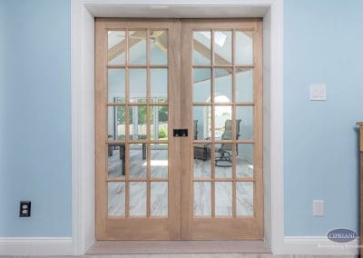 Glass-paneled French doors leading into bright sunroom with vaulted ceiling