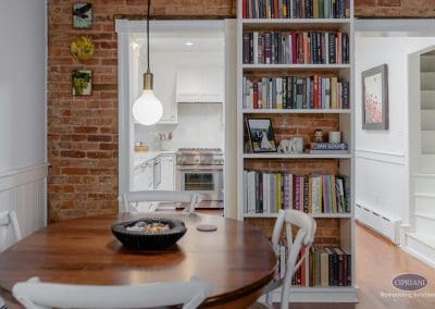 Cozy dining nook with brick accent wall and built-in bookshelves leading to a bright kitchen.