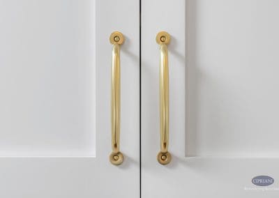 Close-up of two polished gold cabinet handles on white cabinetry.