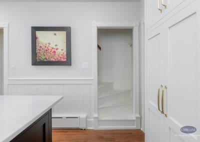 White staircase entry beside kitchen cabinets with gold hardware and floral artwork on the wall.