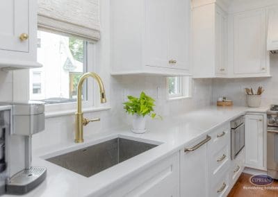 White kitchen sink area with brass faucet, quartz counters, and bright natural light.